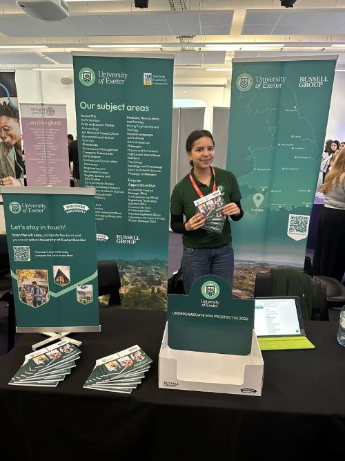 Student working at a booth advertising the University of Exeter